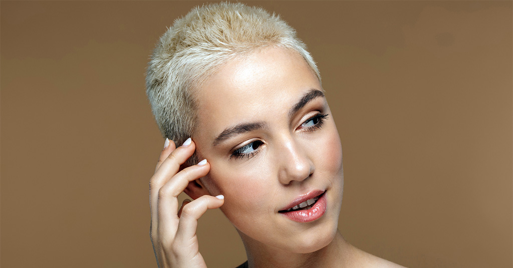 Portrait of a woman with short, bleached blonde hair against a neutral background.