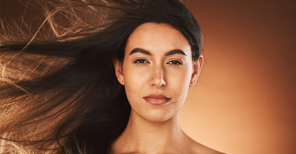 Woman with long dark hair blowing in the wind against a warm brown background.