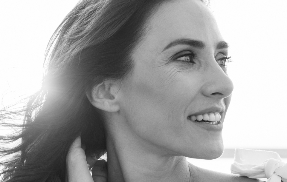 Close-up of a woman smiling and looking to the side with sunlight behind her.