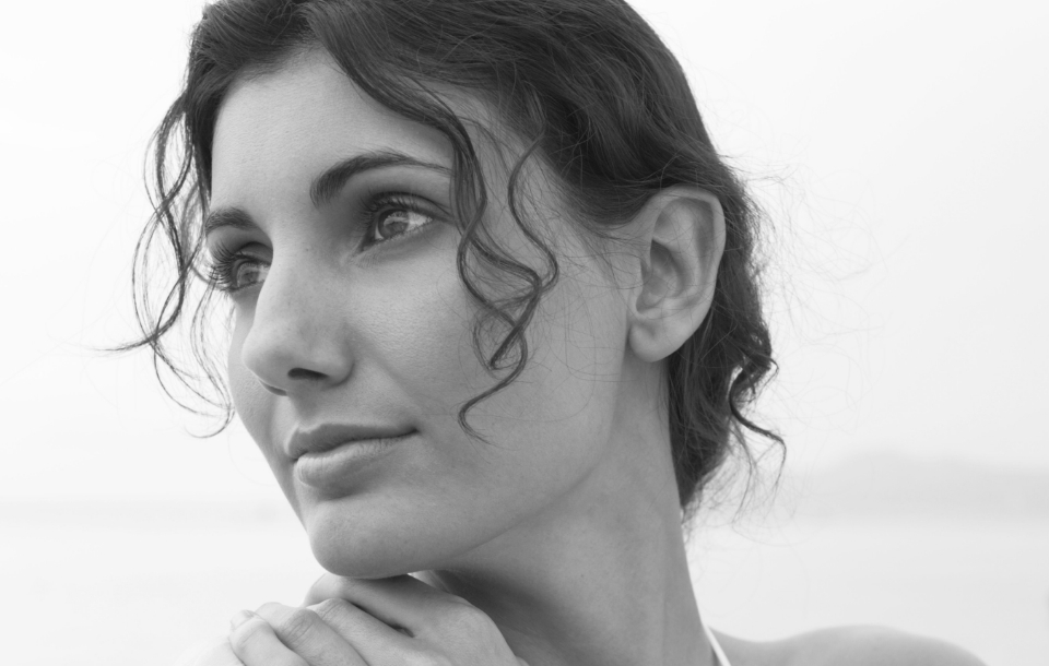 Portrait of a woman with loose curls resting her chin on her hands and gazing thoughtfully into the distance.