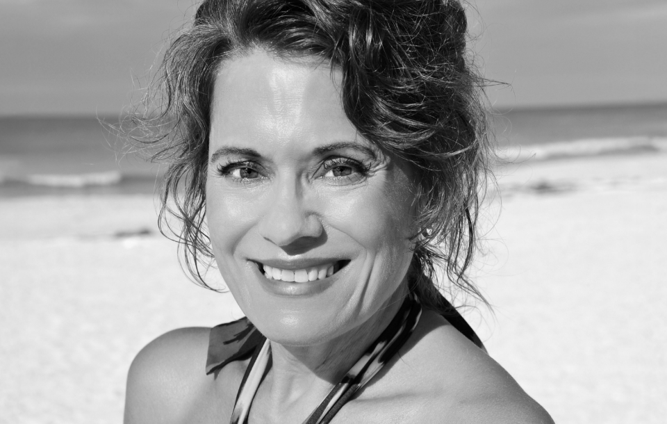 Woman smiling warmly at the beach with the ocean in the background.