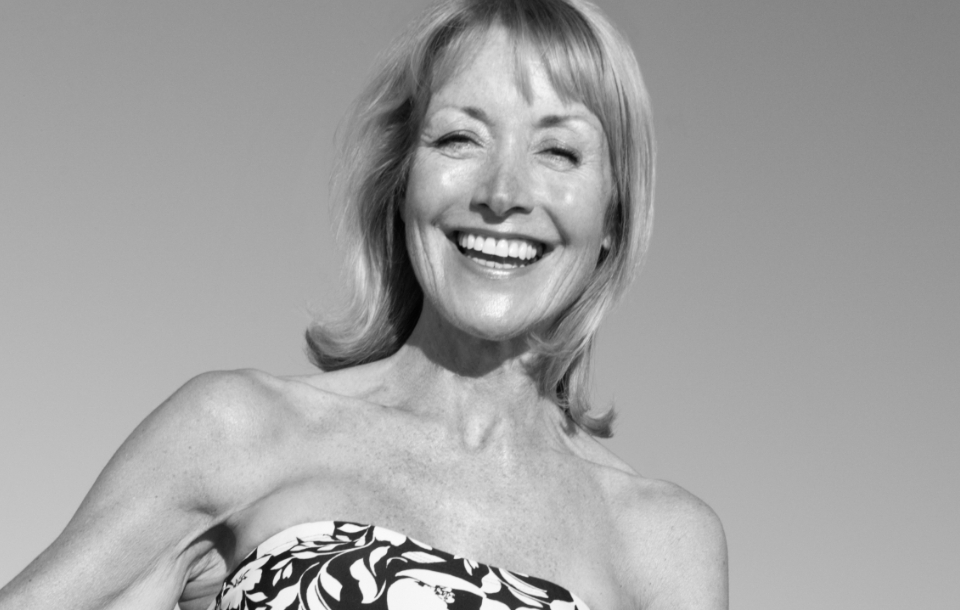 Woman in a strapless patterned top smiling brightly under clear skies.