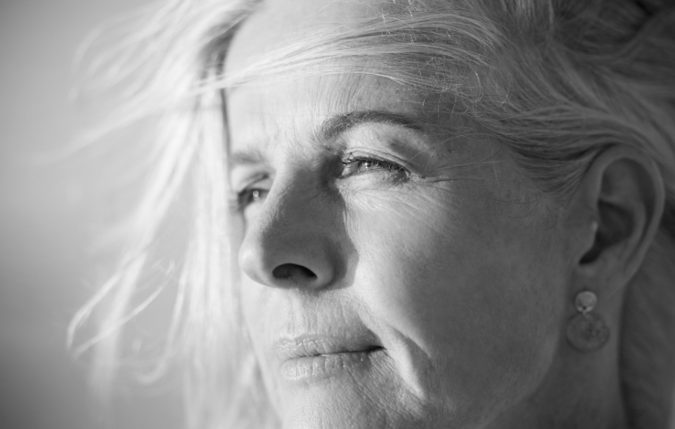 Close-up of a woman with windblown hair gazing thoughtfully into the sunlight.