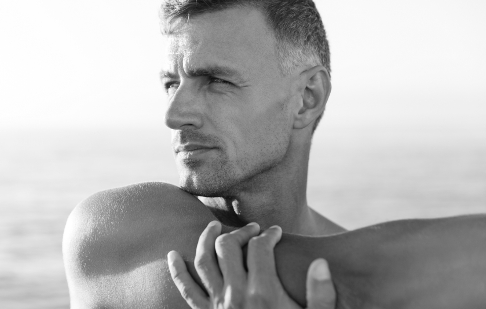 Man standing by the ocean with arms crossed, looking thoughtfully into the distance.