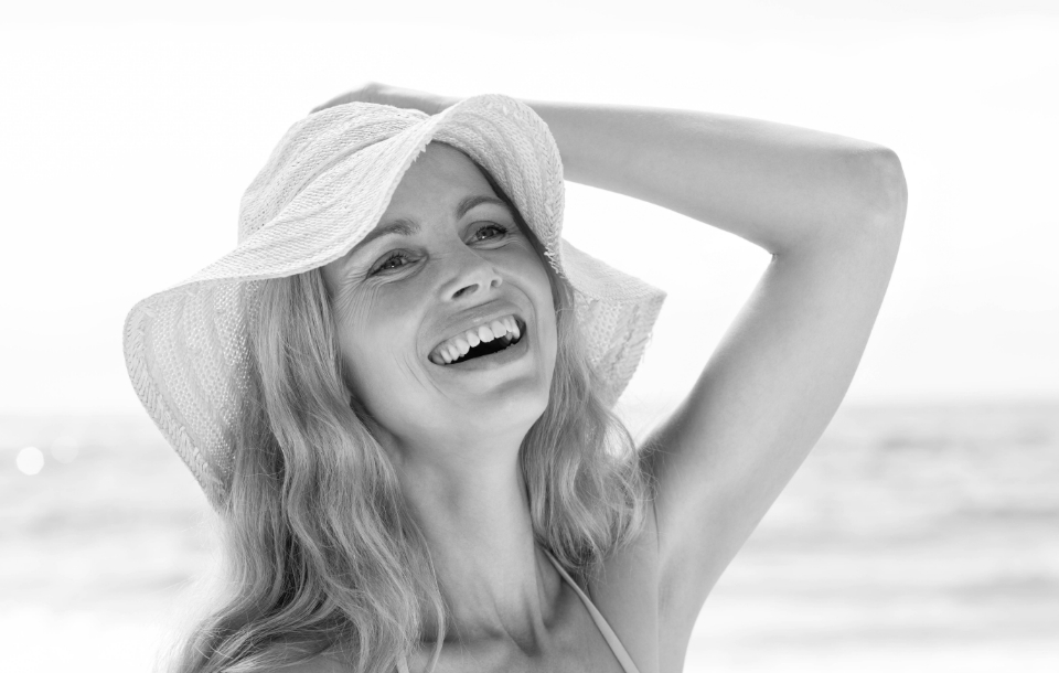 Woman wearing a sun hat laughing joyfully on the beach.