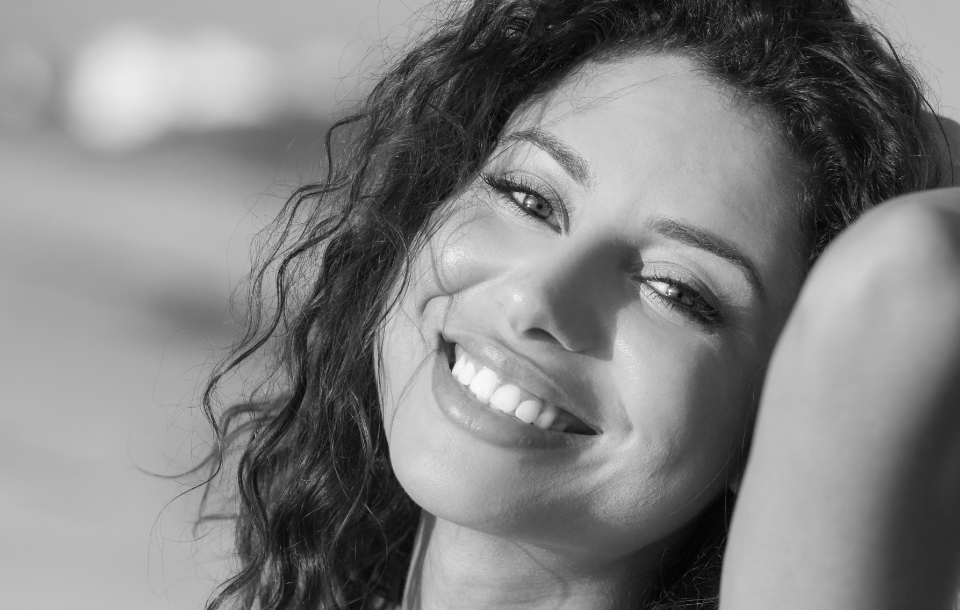 Woman smiling brightly in sunlight, displaying smooth and revitalized skin.