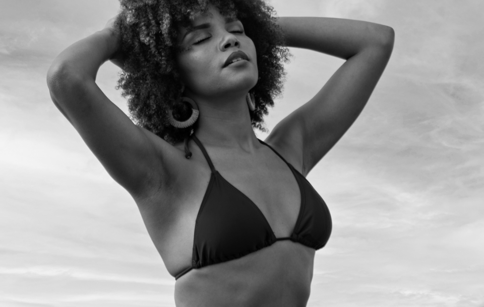 Woman standing with eyes closed and arms raised, revealing smooth, rejuvenated skin.