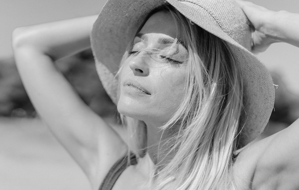 Woman wearing a sun hat with eyes closed, showing clear, refreshed skin.