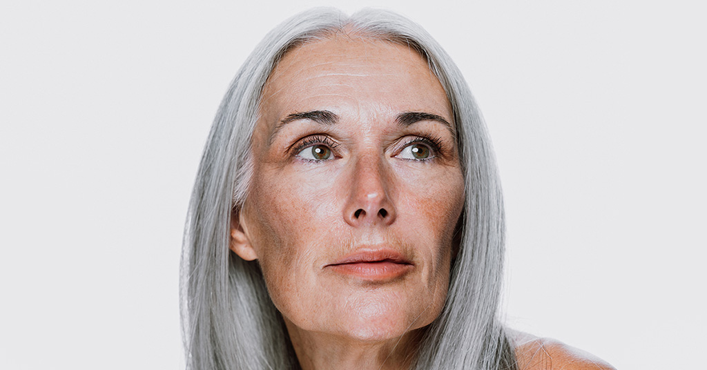 Mature woman with long gray hair looking upward against a plain white background.
