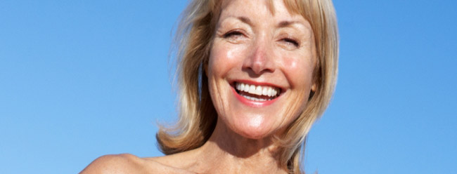 Mature woman smiling brightly under a clear blue sky at the beach.