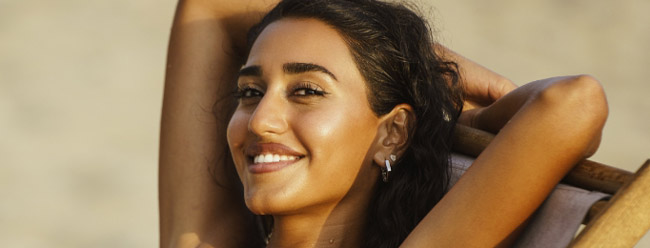 Relaxed woman reclining on a beach chair, smiling with her arms behind her head.