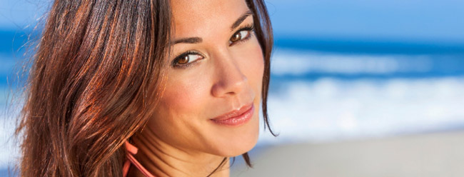 Woman with shoulder-length hair smiling gently with the ocean in the background.