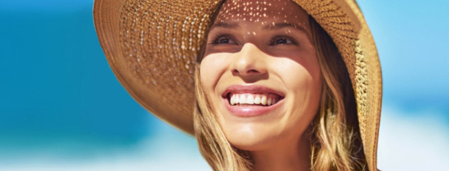 Woman wearing a straw sunhat smiling joyfully under bright sunlight.