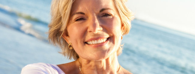 Mature woman smiling warmly on the beach with the waves in the background.