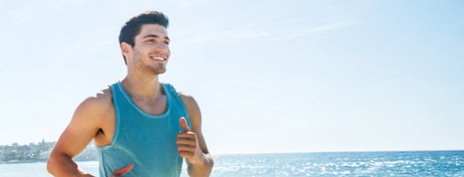 Man jogging along the beach in a blue tank top on a sunny day.