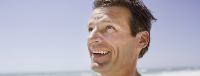 Man looking upward and smiling while standing on a bright, sunny beach.
