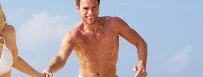 Smiling man running through ocean waves with water splashing around him.