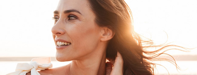 Woman smiling softly with sunlight behind her on a breezy beach.