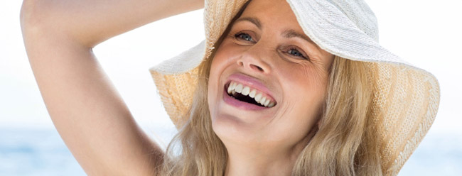 Joyful woman wearing a sunhat and laughing on a bright day near the ocean.