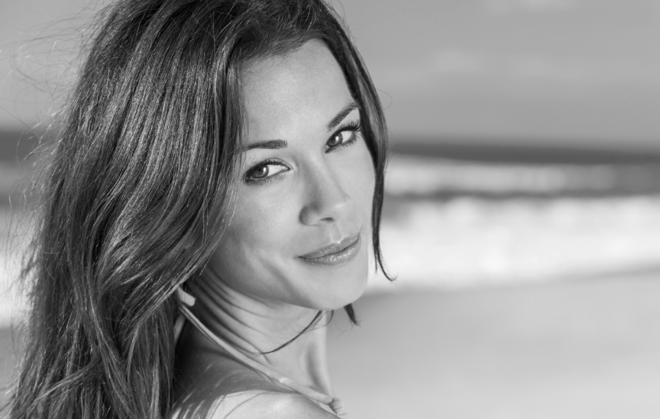Woman smiling softly at the beach, showcasing smooth, radiant skin.