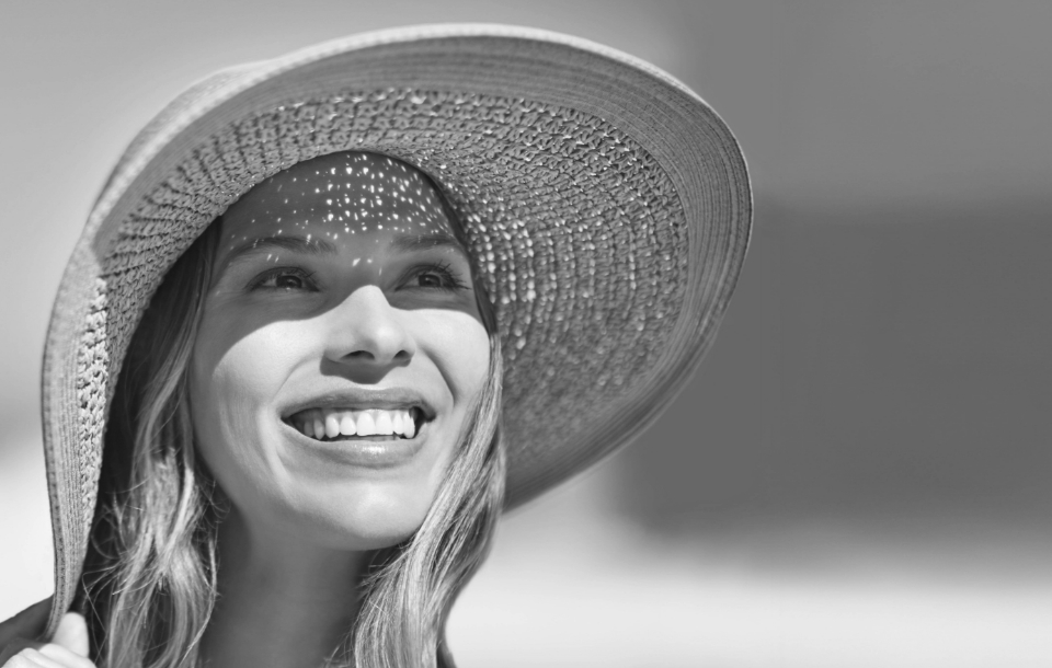 Woman wearing a wide sun hat smiling upward, with luminous, refreshed skin.