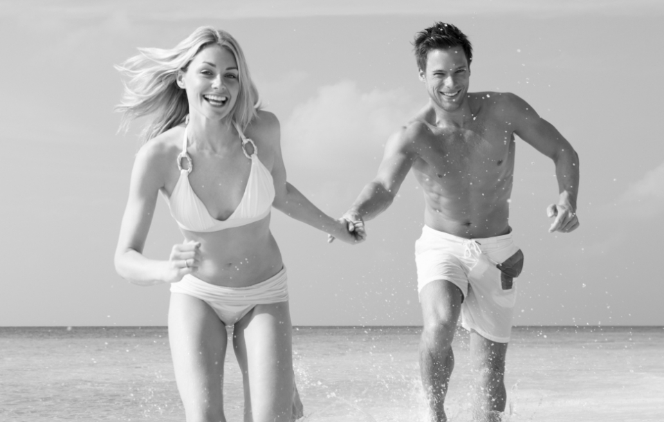 Man and woman smiling as they run through shallow ocean water hand in hand.