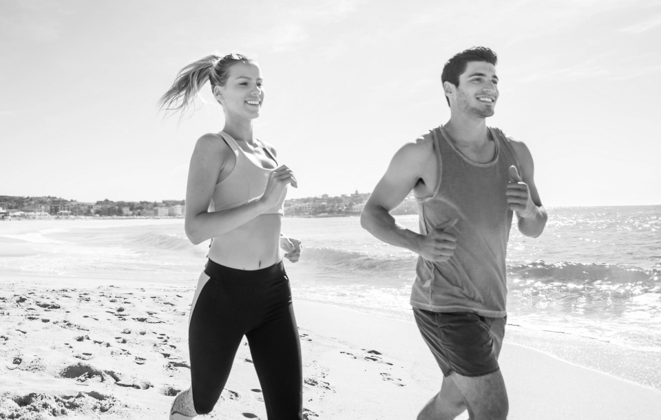 Man and woman jogging along the beach together on a sunny day.